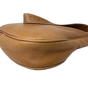 Pu&ograve; includere: Una borsa a tracolla in pelle marrone con un design curvo. La borsa presenta una singola tracolla e cuciture visibili. La pelle ha un aspetto strutturato e la borsa sembra essere vuota.