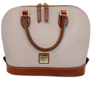 May include: A taupe dome-shaped handbag with brown leather accents. The bag features a top handle, a brown leather base, and gold-tone hardware. The brand name "Dooney & Bourke" is displayed on a small gold plaque.
