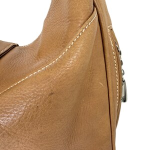Pu&ograve; includere: Primo piano di una borsa in pelle marrone. La borsa ha una superficie strutturata con cuciture bianche lungo le cuciture. Sul lato &egrave; visibile un tirazip argentato. La borsa sembra essere una borsa a spalla o in stile hobo.
