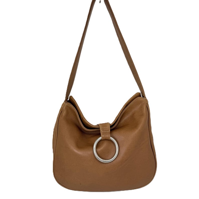 Pu&ograve; includere: Una borsa a tracolla in pelle marrone con una grande chiusura ad anello in metallo argentato. La borsa ha una forma curva e una tracolla lunga e sottile. La pelle sembra liscia e ha una leggera lucentezza. La borsa &egrave; sospesa su sfondo bianco.