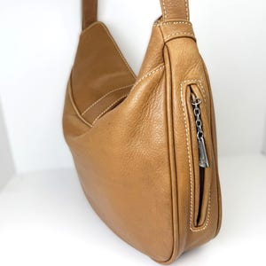 Pu&ograve; includere: Borsa a tracolla in pelle marrone chiaro con un design curvo. La borsa presenta cuciture bianche e una tasca con cerniera con un tirazip argentato. La tracolla &egrave; attaccata in alto e la borsa &egrave; vuota.