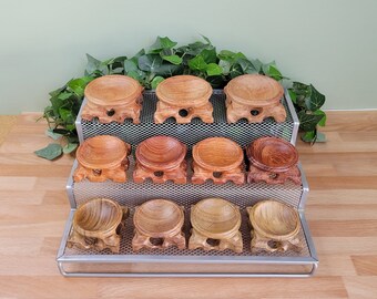 May include: Eleven small, round wooden display stands with carved, pedestal-style bases. Each stand features a concave, bowl-shaped top surface designed for holding objects. The wood displays various natural brown tones, grains, and textures.