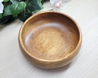 Puede incluir: Un cuenco redondo de madera con un acabado liso y pulido y patrones de grano natural visibles. El cuenco presenta un color marrón medio cálido con vetas más oscuras por toda la madera, mostrando un diseño circular simple.