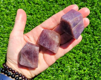 Puede incluir: Tres piedras moradas translúcidas, pulidas e irregulares, con fracturas internas visibles y tonos variados de violeta intenso y lavanda claro. Las piedras tienen superficies lisas y facetadas, mostrando su estructura cristalina natural y formas geométricas.