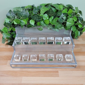 May include: A silver metal tiered display stand with 15 clear glass ring holders. The stand has a mesh design and is empty.