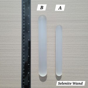 Puede incluir: Dos varitas cil&iacute;ndricas de selenita etiquetadas A y B, colocadas junto a una regla negra. La varita B mide aproximadamente 21,5 cm de largo, mientras que la varita A mide aproximadamente 18 cm. Ambas son de color blanco transl&uacute;cido con extremos redondeados.