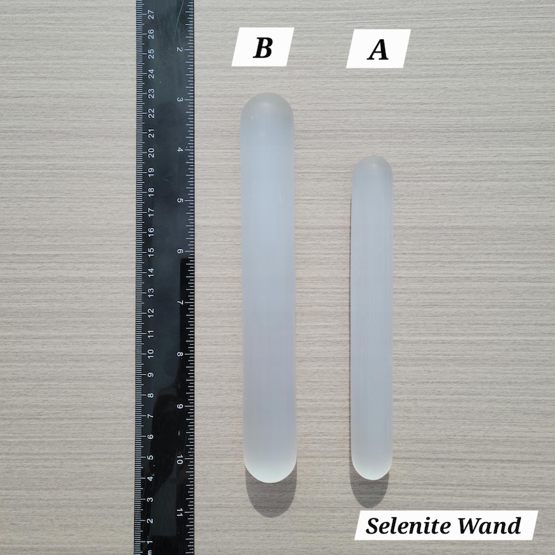 Puede incluir: Dos varitas cil&iacute;ndricas de selenita etiquetadas A y B, colocadas junto a una regla negra. La varita B mide aproximadamente 21,5 cm de largo, mientras que la varita A mide aproximadamente 18 cm. Ambas son de color blanco transl&uacute;cido con extremos redondeados.