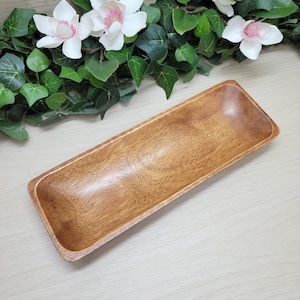 May include: A rectangular wooden tray with a smooth, polished finish and visible natural grain patterns. The tray features slightly curved sides and rounded corners, showcasing a warm, medium-brown tone throughout the entire surface.