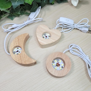 May include: Three wooden LED light bases in the shapes of a crescent moon, a heart, and a circle. Each base has a small LED light and a white USB cable with an on/off switch. The wood has a natural, light brown color.