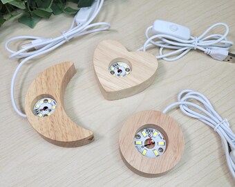 May include: Three light-colored wooden display bases in heart, crescent moon, and circular shapes. Each base features a circular LED light insert in the center and is connected to a white USB power cord with an integrated inline switch.