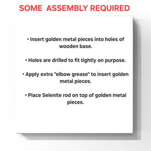 Puede incluir: Una tarjeta de instrucciones blanca con texto rojo en la parte superior que dice SOME ASSEMBLY REQUIRED. El texto negro enumera cuatro pasos: Insertar piezas met&aacute;licas doradas en los agujeros de la base de madera. Los agujeros est&aacute;n perforados para un ajuste apretado. Aplicar fuerza extra para insertar las piezas doradas. Colocar la varilla de selenita sobre las piezas doradas.