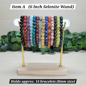 Puede incluir: Un soporte de exhibici&oacute;n de varita de selenita de 15,24 cm con base de madera clara y soportes de metal dorado. El soporte sostiene 14 pulseras de cuentas de piedras preciosas multicolores, con cuentas de 8 mm en negro, rojo, morado, azul, verde y amarillo.