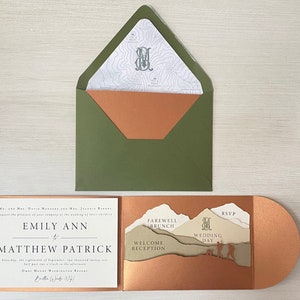 Puede incluir: Una invitación de boda con un diseño de cordillera montañosa. La invitación está doblada por la mitad y tiene un sobre de color cobre. El texto de la invitación dice "Emily Ann a Matthew Patrick" y "Despedida Brunch, Recepción de Bienvenida, Día de la Boda".