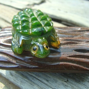 May include: A green glass turtle figurine with a textured shell, sitting on a brown wooden log. The turtle has realistic details, including eyes and feet.