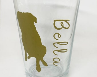 Könnte beinhalten: Ein klares Glas mit einer goldenen Silhouette eines Hundes und dem Namen "Bella" in goldenen Buchstaben.