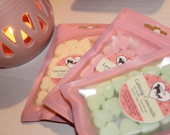 Könnte beinhalten: Drei Beutel mit herzförmigen Wachsschmelzen in rosa Verpackung. Die Beutel sind mit "Luscious Lavender", "Lavender Petals" und "Calming Chamomile" beschriftet.
