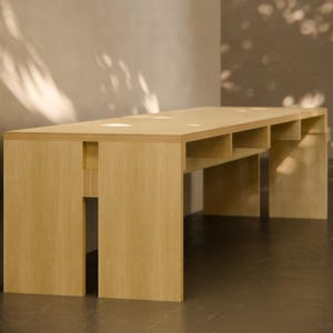 May include: A light wood table with a simple design and open shelves. The table is made of plywood and has a natural finish.