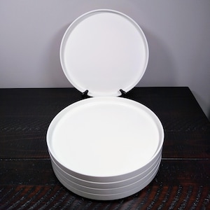 May include: A stack of five white ceramic plates, with one plate standing upright behind the stack.