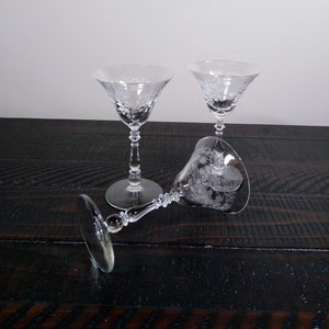 May include: Two clear glass stemmed cocktail glasses with etched floral designs. The glasses are on a dark wood surface.