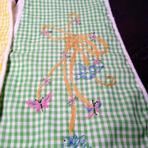 May include: Green and white gingham patterned kitchen towel with embroidered butterflies and birds. The embroidery features a gold bow, pink butterflies, and blue birds. The towel has a white border.