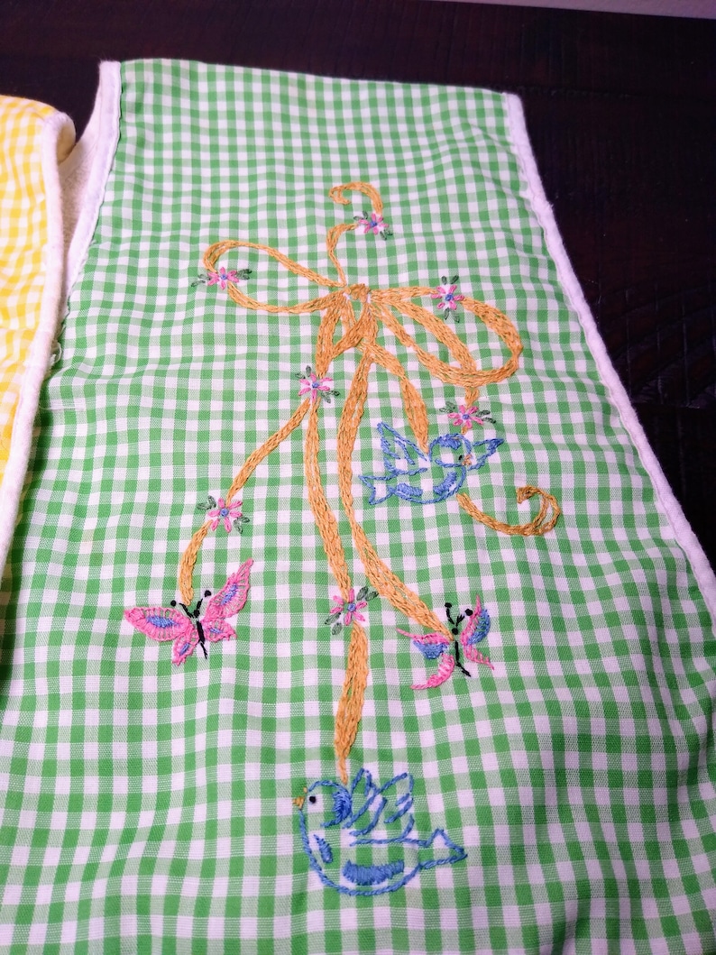 May include: Green and white gingham patterned kitchen towel with embroidered butterflies and birds. The embroidery features a gold bow, pink butterflies, and blue birds. The towel has a white border.