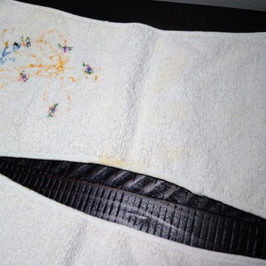 May include: White terry cloth towel with embroidered floral designs in blue, pink, and yellow. The towel has a slightly textured surface and shows some discoloration.