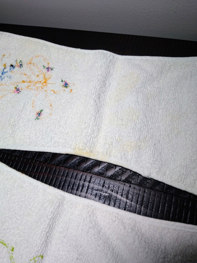 May include: White terry cloth towel with embroidered floral designs in blue, pink, and yellow. The towel has a slightly textured surface and shows some discoloration.
