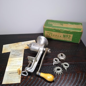 May include: An antique Universal Food Chopper No. 2, made of silver metal, with a wooden handle. Includes a green box and several cutting attachments. A vintage kitchen tool for grinding meat and food.