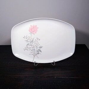 May include: White rectangular serving platter with a pink rose and gray floral design. The platter is supported by a metal stand. The rose is on the left side of the platter.