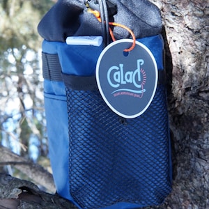Puede incluir: Una bolsa de cordón azul con un bolsillo de malla negra y una etiqueta negra y blanca que dice "Calac" con el texto "surf adventures gear".