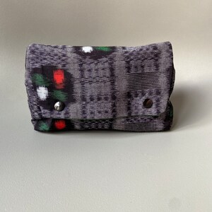 May include: A small black and gray patterned fabric pouch with red, green, and white accents. The pouch has a flap closure and two silver snaps.