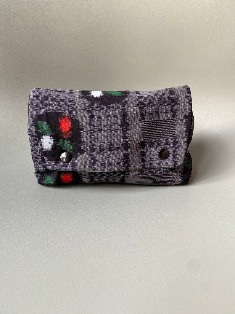 May include: A small black and gray patterned fabric pouch with red, green, and white accents. The pouch has a flap closure and two silver snaps.
