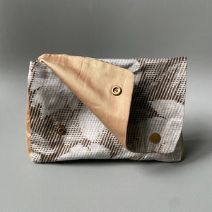 May include: A small, beige and white patterned clutch with a flap closure and gold-toned snap buttons.
