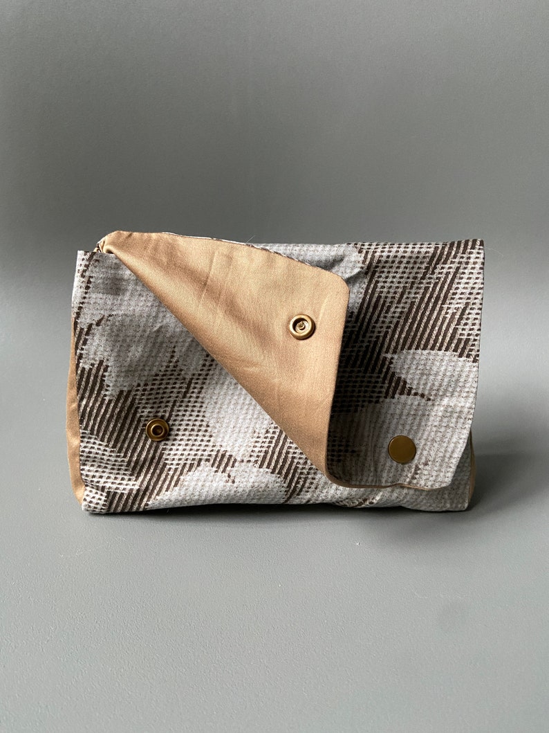 May include: A small, beige and white patterned clutch with a flap closure and gold-toned snap buttons.