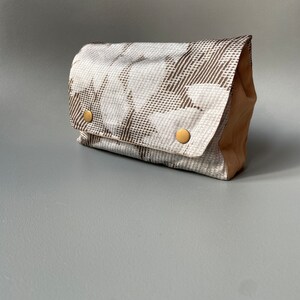 May include: A small, rectangular clutch bag with a brown and white geometric pattern. The bag has a flap closure and two gold-toned buttons.