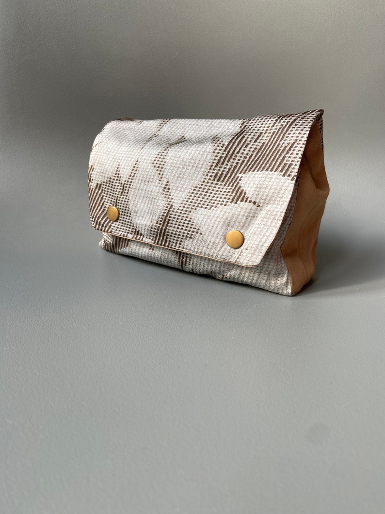 May include: A small, rectangular clutch bag with a brown and white geometric pattern. The bag has a flap closure and two gold-toned buttons.