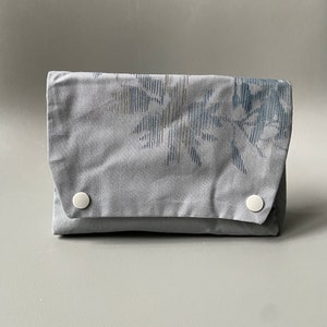 May include: A gray fabric pouch with a floral pattern and two white buttons.