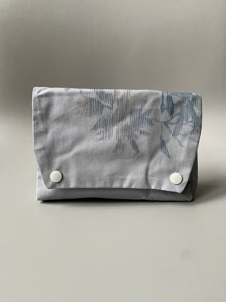May include: A gray fabric pouch with a floral pattern and two white buttons.