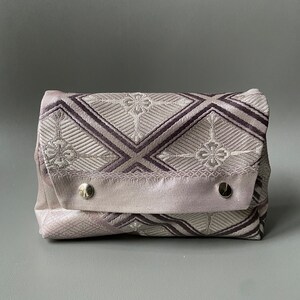 May include: A small, rectangular, gray and white patterned pouch with a flap closure and two silver snaps. The pouch is made of a soft, textured fabric.