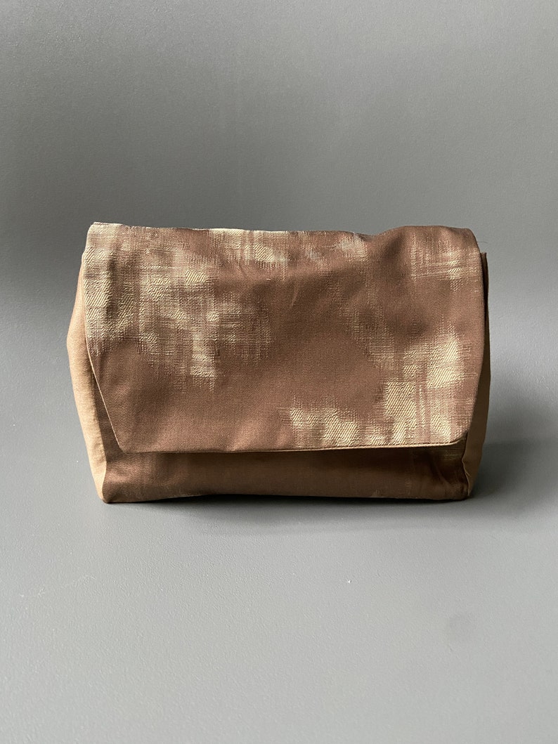 May include: A brown clutch purse with a white pattern. The purse has a flap closure and a soft, textured fabric.