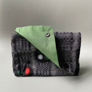 May include: A black and green fabric clutch with a green flap and snap closure. The clutch has a geometric pattern and a red accent.
