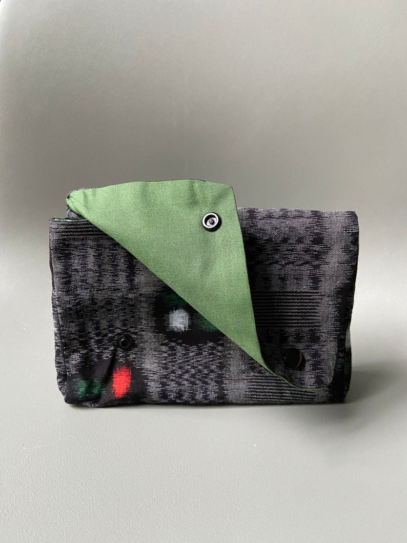 May include: A black and green fabric clutch with a green flap and snap closure. The clutch has a geometric pattern and a red accent.