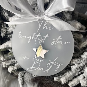 May include: A white frosted glass ornament with a silver star and the text "The brightest star in our sky Dad".