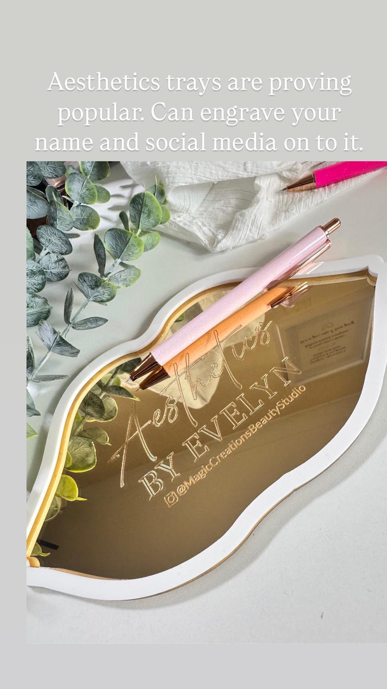 May include: A gold-colored, lip-shaped tray with a white border. The tray has the words "Aest" and "BY EVELYN" engraved on it, along with the social media handle "@MagicCreationsBeautyStudio".