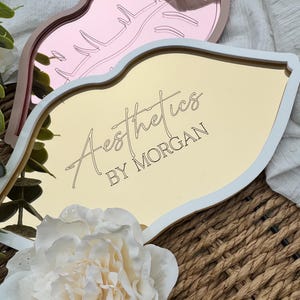 May include: Gold and pink lip-shaped trays with white trim. The gold tray has the text "Aesthetics by Morgan" on it.