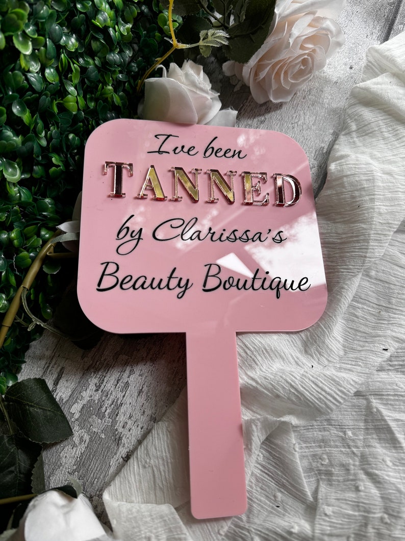 May include: Pink acrylic sign with the text "I've been TANNED by Clarissa's Beauty Boutique" in gold letters.