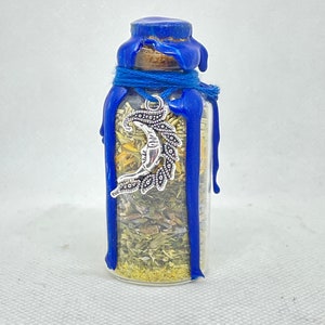 May include: A small glass bottle filled with dried herbs and sealed with blue wax. A silver crescent moon charm hangs from the top of the bottle.