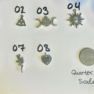 May include: Eight silver charm pendants with various designs, including a pentagram, a triquetra, a crescent moon, a sun, a heart, a fairy, and a crescent moon with a fairy. A US quarter is included for scale.