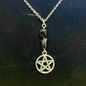 Peut inclure: Un collier en cha&icirc;ne argent avec un pendentif pentagramme argent et deux perles noires.