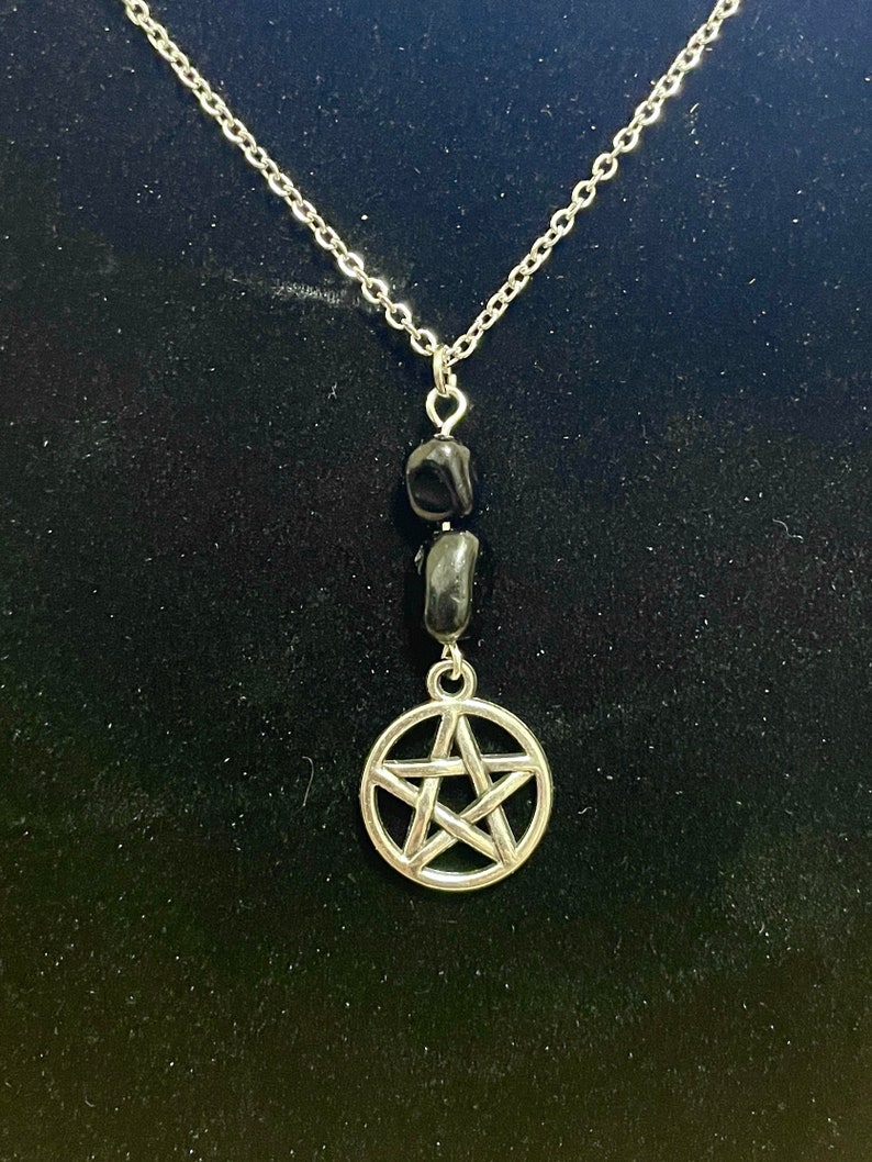 Peut inclure: Un collier en cha&icirc;ne argent avec un pendentif pentagramme argent et deux perles noires.